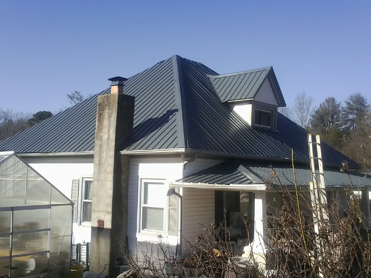 Dark blue standing seam metal roof on a white farmhouse with dormer — Slate & Tile Roof Repair by Roofing Brothers in Beaver Meadows