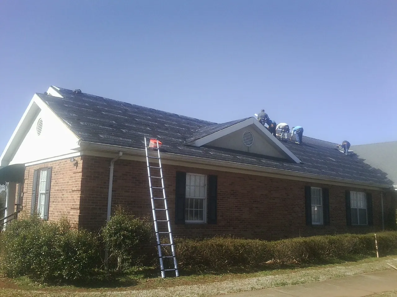 Crew tearing shingles off a brick ranch roof with a ladder set — Metal Roof Repair work by our crew in Beaver Meadows