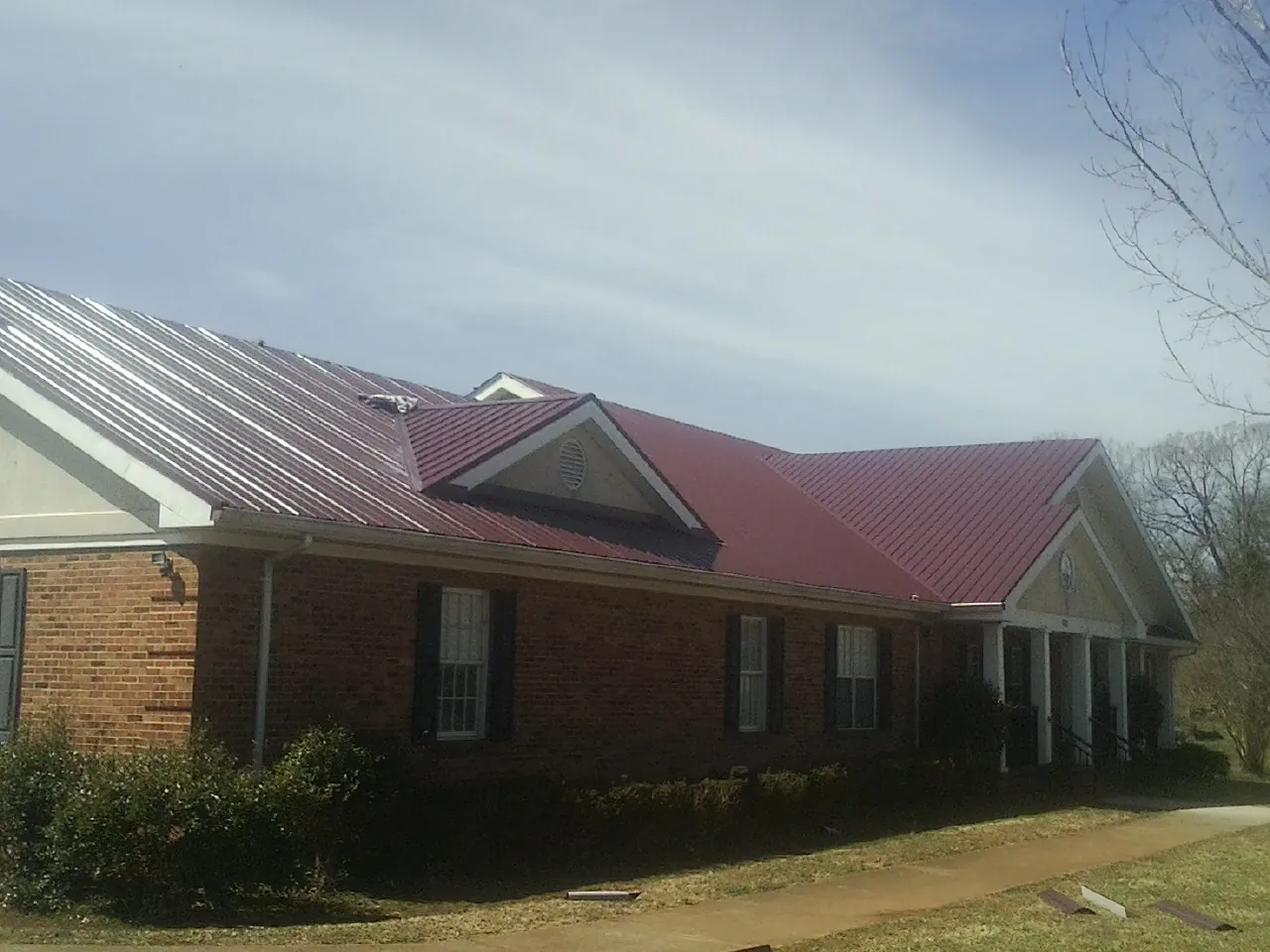 Red metal roof with gabled entries on a long brick building, from a Hail Damage Roof Repair job in Beaver Meadows