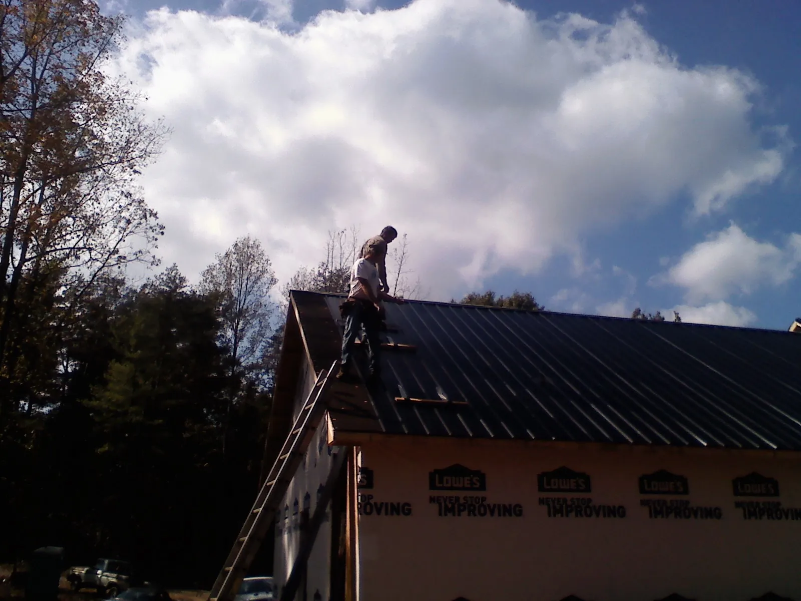 Roofer fastening dark metal panels high against a cloudy sky, from a Roof Inspection job in Beaver Meadows
